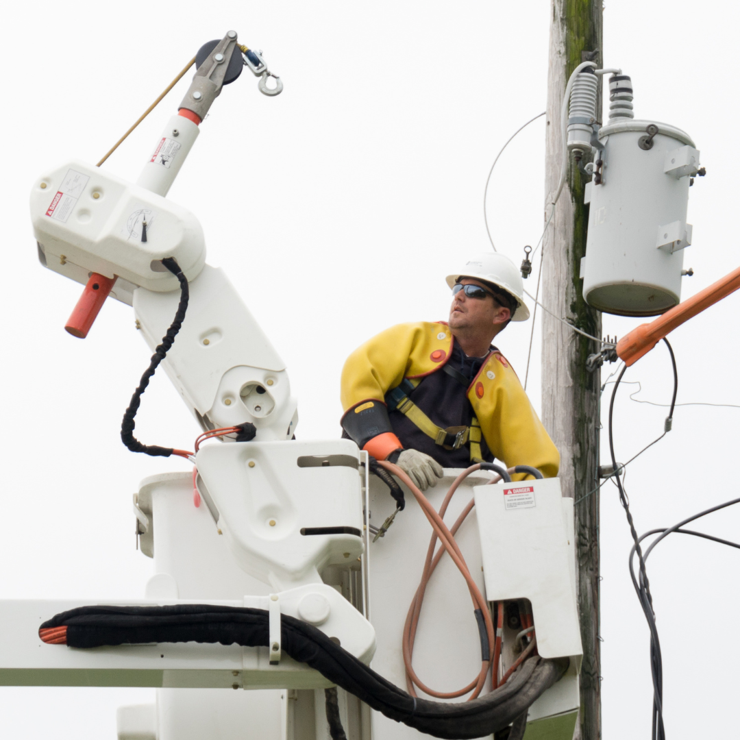 Picture shows an electric line worker in a bucket making repairs to electric lines.